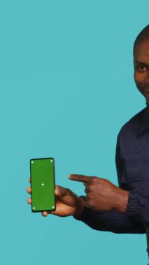 Yeşil ekran akıllı telefon gösteren neşeli güvenlik elemanının dikey video portresi. Neşeli devriye acentesi güvenli bir ortam sağlıyor. Model telefon, stüdyo geçmişi, kamera A.