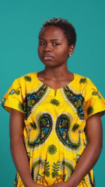 Dikey Video Genç doğal kadın stüdyoda hem sağa hem de sola bakıyor, çevreyi ve çevresini kontrol ediyor. Sıradan bir kız geleneksel Afrika kıyafetleri giyer.