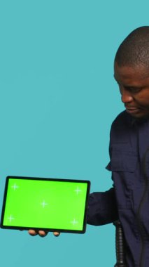 Güvenlik ajanının dikey video portresi kroma anahtar tableti sunuyor ve atölye arkaplanını güvene alıyor. Gardiyan, güvenlik ihlalleriyle uğraşırken izole ekran cihazını işaret ediyor