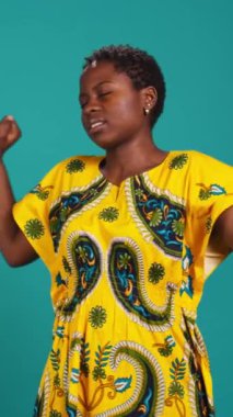 Dikey Video Gündelik Genç Yetişkin Esneme ve Rahatlama Stüdyoda, Çiçeksel yerli unsurlarla geleneksel bir kıyafet giyerek. Kendine güvenen neşeli kadın sırtını düzeltiyor, duruşunu düzeltiyor.