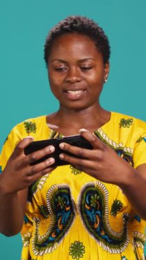 Vertical Video Neşeli Kadın Oyuncu stüdyoda mobil video oyunları oynuyor, akıllı telefon uygulamasında modern eğlence aktiviteleriyle eğleniyor. Gülümseyen kişi çevrimiçi oyun turnuvalarından hoşlanıyor. Kamera A.