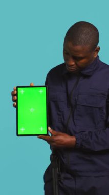 Dikey video Mutlu güvenlik görevlisi koruma görevi sunumu tablet. Neşeli korumanın portresi yeşil ekran cihazı, stüdyo arka planında izole edilmiş, kamera B
