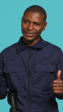 Neşeli güvenlik görevlisinin dikey video portresi. İşaret işareti yapıyor. Parmak işareti yapıyor. Özel polis memuru olumlu el hareketi yapıyor, stüdyo arkaplanı.