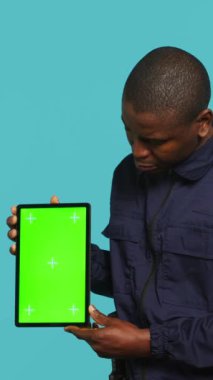 Dikey video Mutlu güvenlik görevlisi koruma görevi sunumu tablet. Neşeli korumanın portresi yeşil ekran cihazı, stüdyo arka planında izole edilmiş, kamera A