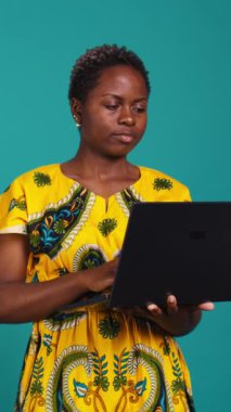 Stüdyodaki bir dizüstü bilgisayarda web sitelerini karıştıran düşünceli bir kadın sosyal medya sayfalarını kontrol etmek için internet ağına bağlanıyor. Serbest çalışmak için elinde kablosuz bilgisayar tutan genç bir yetişkin.