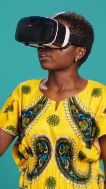 Mavi arka planda VR gözlükleri kullanarak sanal gerçeklik cihazıyla yüksek teknoloji deneyimi olan dikey video harikası bir kız. Akıllı kulaklık kullanan genç bir kadın. Kamera A.
