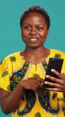 Vertical Video Friendly olumlu kadın akıllı telefonuyla online video görüşmeleri yapıyor, webcam 'e el sallıyor ve stüdyodaki arkadaşlarıyla sohbet ediyor. Gülümseyen tatlı kız gündelik bir konuşma yapıyor.