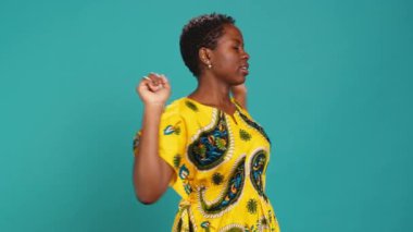 Stüdyoda sırt ve kol kaslarını esneten doğal tatlı bir kadın, mavi arka planda rahatlıyor ve duruşunu düzeltiyor. Afrikalı etnik kökenini temsil eden genç bir kadın. Kamera A.