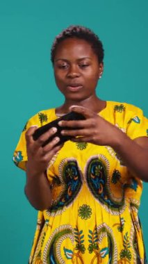 Vertical Video Happy bir online video oyunu yarışmasını kazanan kızı memnun etti, mavi arka planda e-spor turnuvasında oynarken eğlendi. Kadın internet oyunu oynuyor, zaferini kutluyor. Kamera B