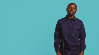 İzinsiz girenleri tahliye etmekle görevli güvenlik görevlisinin portresi, ateş ediyormuş gibi yapmak. Devriye aracı çevreyi koruyor, el kol hareketleri yapıyor, stüdyo arka planı, kamera B