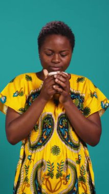 Dikey Video Neşeli, mavi arka planda bir fincan kahve içen neşeli kişi, stüdyoda kızarmış aroma ve tazeliğin tadını çıkarıyor. Kafein servisi yapan tatmin olmuş bir kadın. Kamera B.