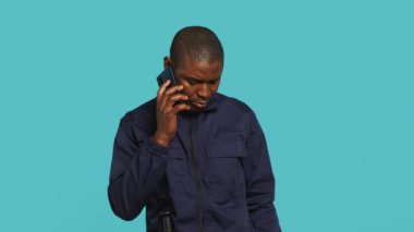 İşyerindeki güvenlik görevlisinin portresi mekanı denetlerken arkadaşlarını aramak için telefon kullanıyor. Özel güvenlik görevlisi arkadaşlarıyla telefon görüşmesi yapıyor, stüdyo arkaplanı, kamera A