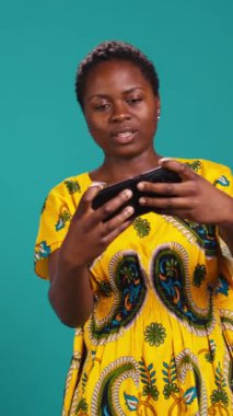 Vertical Video Neşeli Kadın Oyuncu stüdyoda mobil video oyunları oynuyor, akıllı telefon uygulamasında modern eğlence aktiviteleriyle eğleniyor. Gülümseyen kişi çevrimiçi oyun turnuvalarından hoşlanıyor. Kamera B.