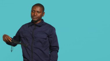 Güvenlik ajanının portresi atanmış bir görevi güvence altına alıyor, göz korkutucu görünmesi için sopayla eline vuruyor. Gardiyan, güvenlik ihlali ve kamera A ile tehdit jesti yapıyor.