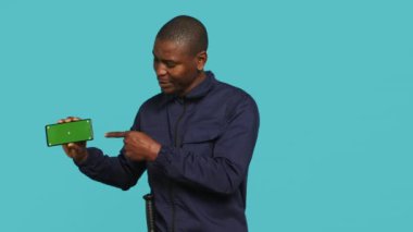 Korumada çalışan neşeli güvenlik görevlisi kroma anahtar cep telefonunu sunuyor. Neşeli korumaların portresi izole edilmiş cep telefonu, stüdyo arka planında izole edilmiş, kamera A