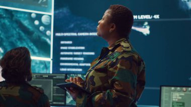 Uydu görüntüleme uzmanı kadın yüksek teknoloji uzmanı büyük ekranda yeni bir ulusal güvenlik görevi için askerleri hazırlıyor. Komuta merkezindeki kadın üsteğmen. Kamera A.
