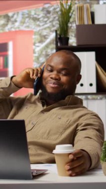 Dikey Video Küçük işletme sahibi telefon konuşmasında yeni genişleme projesi hakkında konuşuyor, yatırımcılarla finansmanı artırmak için pazarlık yapıyor. Ekonomik analiz ve finans yönetimi için dizüstü bilgisayar kullanmak