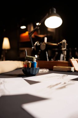 Masa, kağıt üzerinde moda tasarımları ve terzilik stüdyosunda dikiş aletleriyle dolu. Eskiz çizimleri, iplik makaraları, dikiş makinesi olan profesyonel atölye çalışma alanı
