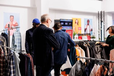 Giyim mağazasında durup indirimli fiyattan kıyafet seçen bir grup insan. Kara Cuma satışlarında müşteriler çıldırıyor, sezonluk moda indirimleri sırasında kelepir mal arıyorlar.