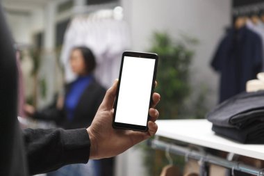 Alışveriş merkezi alıcısı elinde akıllı telefonla boş ekranı tutuyor, internette ve butikte giyim kuşamını tarıyor. Kıyafet mağazası müşterisi terfi için boş dokunmatik ekranlı cep telefonu kullanıyor
