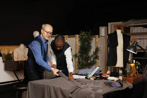 stock image Experienced dressmakers cutting fabric, manufacturing stylish sleek business clothing in refined masterful craftmanship. Tailors working with textile materials in atelier shop, creating bespoke attire