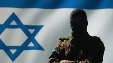 Maske takan Mossad operatörü İsrail bayrağı önünde gururla duruyor ve ülkesine hizmet etmekten gurur duyuyor. İsrail gizli ajanı kumanda odasında çapraz silah, kamera B