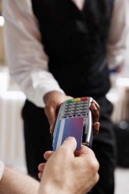 Kafkasyalı yaşlı bir adamın dinlenme odasındaki garsonun tuttuğu ödeme makinesinden kredi kartını çekerken çekilmiş fotoğrafı. Detaylı görüntü, otel lobisindeki rezervasyon için Po terminalinde ödeme yapan birini gösteriyor..