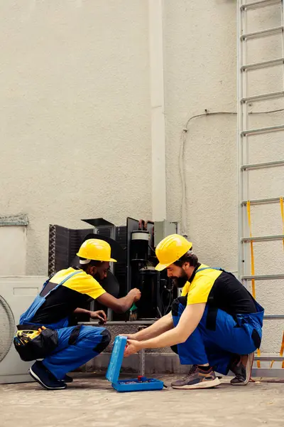 stock image Professional engineer using soft dusting brush to sweep away built up layer of dirt and debris from condenser coil while licensed serviceman refills cooling system refrigerant tank