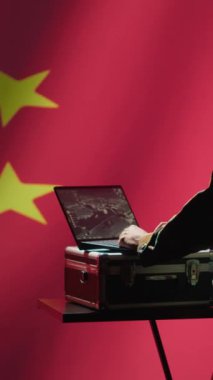 Dikey video Çin ordusu askeri harekat subayı laptoptaki gözetleme yayınına bakıyor, askerlere kulaklık kullanarak bilgi aktarıyor, dalgalanan Çin bayrağı arka planında izole edilmiş, kamera A