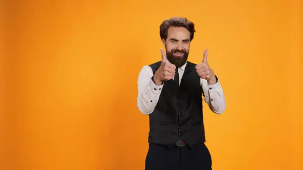 stock image Staff member gives thumbs up while appearing happy and optimistic in studio. Waiter standing proudly and showing okay signal on camera, server making positive acceptance gesture.