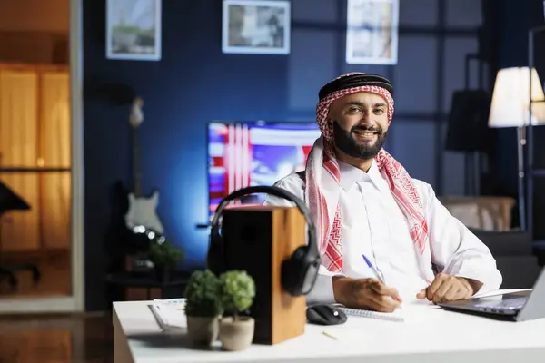 stock image Portrait shot of Muslim man freelancer using laptop to browse the internet while carrying a pen. Side-view of Arab guy looking at camera, displaying his professional profile in contemporary workplace.