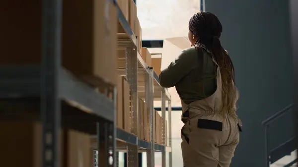 stock image Chief logistics officer in warehouse arranging cardboard boxes full of merchandise ready to be shipped to clients. Meticulous director in depository using ladder to put parcels on cabinet shelves