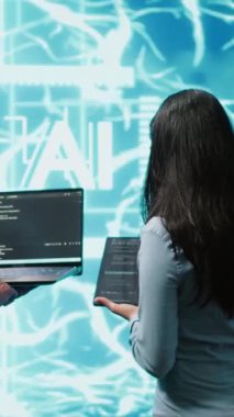 Yapay zeka sinir ağlarını korumak için tablet ve dizüstü bilgisayar kullanan dikey video ekibi. Ekip çalışanları AI sistemini kullanarak işlemlere ve aktarımlara yardım ediyor