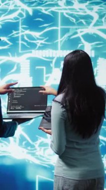 Dikey video çalışanları beyin fırtınası yapıyor, yapay zeka sinir ağlarını onarmak için cihazlar kullanıyorlar. Yüksek teknolojili çalışma alanı meslektaşları yapay zeka sistemini kullanarak işleme ve iletime yardımcı oluyorlar.