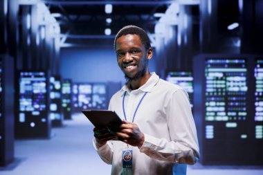 Portrait of engineer in front of operational mainframes in high performance computing server room. Specialist monitoring equipment energy consumption, ensuring ideal operations conditions clipart