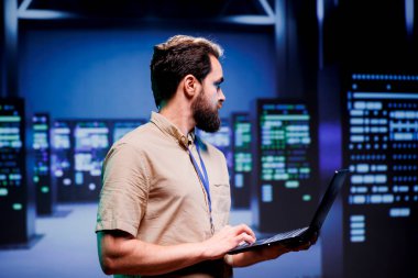 Bilgi işleme platformları, depolama cihazları ve ağ aygıtları depolama sunan sunucu merkezindeki IT geliştiricisi çok miktarda bilgisayar kaynağı sunuyor. Çalışan dizüstü bilgisayarla altyapı bakımı yapıyor.