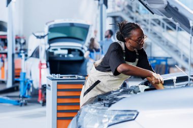 Araba servisindeki Afrikalı Amerikalı kadın bozuk radyatörü tamir etmek için profesyonel mekanik aletler kullanıyor. Otomobil tamirinde deneyimli bir tamirci, en iyi otomotiv performansını sağlıyor