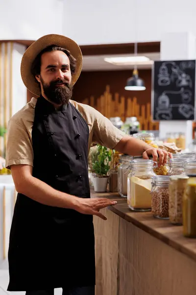 stock image Portrait of smiling zero waste shop seller next to organic ecofriendly pantry staples jars. Cheerful man working in environmentally conscious local neighborhood store selling sustainable products