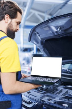 Garajda uzman bir teknisyen, arabanın bakımını yaparken kontrol listesini takip etmek için dizüstü bilgisayar kullanıyor. Otomobil tamir atölyesindeki yetenekli işçiler, izole ekran cihazının yardımıyla aracın kontrolünü yapıyor