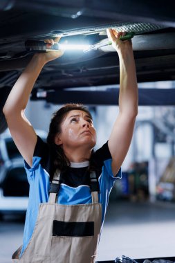 Garajda çalışan çalışkan bir tamirci rutin bakım sırasında lastikleri kontrol ediyor. Aracın altındaki tamirhanede çalışan çalışkan bir tamirci, iş ışığı kullanarak kontrol ediyor.