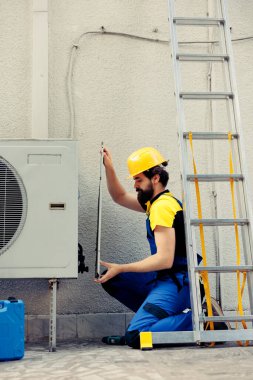 Sertifikalı elektrikçi, metal bobin panelini açmak için el matkabı kullanarak bozuk klima üzerinde çalışmaya başlıyor. İçerideki enkazı kontrol etmek için hvac sistemi açmaya yetkin tamirci