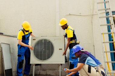 Becerikli işçiler müşteri için yeni bir klima kuruyor. Afrikalı Amerikalı iş arkadaşları olan yetenekli elektrikçi yeni HVAC sistem etkinliğini optimize etmek için görevlendirildi