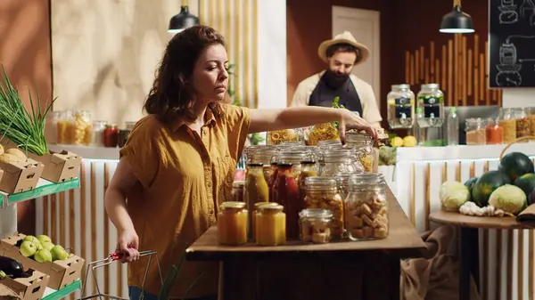 stock image Vegan woman in specialty zero waste supermarket using shopping basket to purchase bulk items in easily repurposable jars. Client in local neighborhood shop buying pesticides free natural food