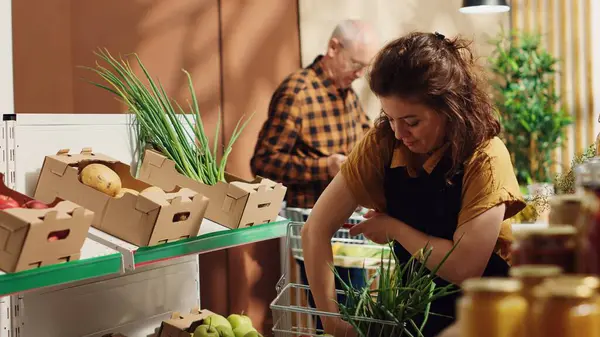 stock image Woman working in zero waste supermarket refilling shelves with fresh produce. Storekeeper shelving recently arrived freshly harvested vegetables in local neighborhood store