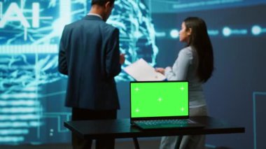 Takım çalışanı yapay zeka teknisyenleri iş veri analizi için yeşil ekran laptop kullanıyorlar. Bilişim uzmanlarından oluşan bir ekip yapay zeka ve kamera A kullanarak görevleri otomatik hale getirmek için model defter üzerinde çalışıyor.