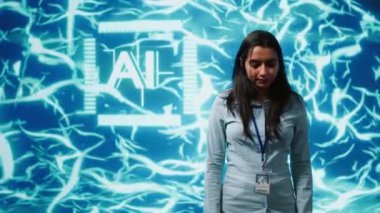 Gülümseyen bilişim uzmanının portresi, yapay zeka ve sinirsel ağ grafiklerinin yer aldığı ileri teknoloji ekranı önünde kollarını kavuşturarak duruyor. Yapay zeka alanında gelişme kaydeden araştırmacı, kamera A