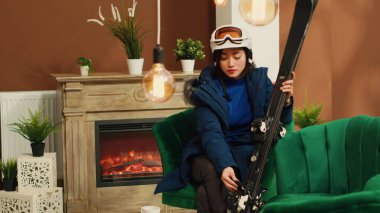 Asyalı biri kış aktivitelerine hazırlanıyor ve dağ kayak merkezinin lobisinde oturmuş kayak ve miğferleri kontrol ediyor. Kış sporu hayranı alp yamaçlarda kayak yapmaya hazırlanıyor..