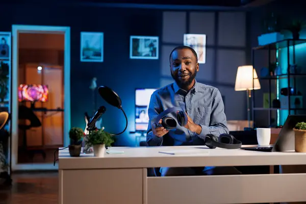 stock image Audio engineer comparing headphones in different price ranges, filming from dimly lit home studio. Viral tech content creator showing listening devices to fans, doing review