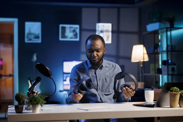 stock image Content creator in dimly lit living room uses camera to film wireless headphones review, unhappy with subpar sound quality. Online star disappointed by weak maximum volume on music listening