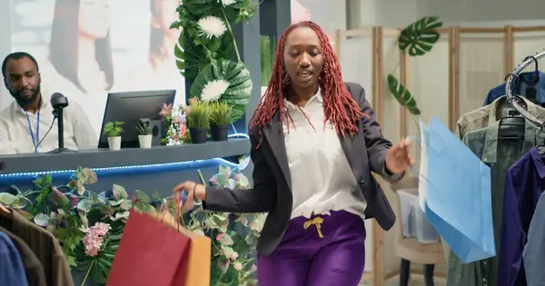 Stock image African american woman dancing with shopping bags in hand while thrifting in vintage clothes shop. Customer enjoying herself premium second hand clothing store after finding hidden gems